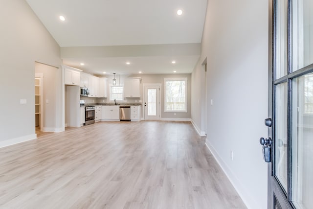 unfurnished living room with sink, high vaulted ceiling, and light hardwood / wood-style flooring