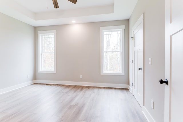 unfurnished room featuring ceiling fan, light hardwood / wood-style floors, and a tray ceiling