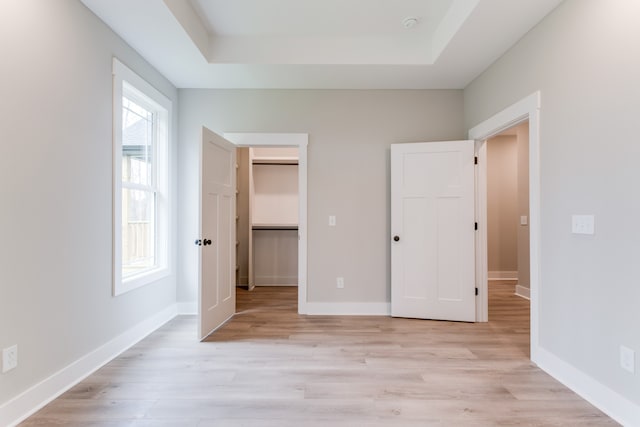 unfurnished bedroom with light hardwood / wood-style floors, a spacious closet, and a tray ceiling