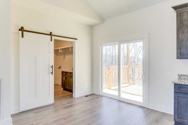 interior space with vaulted ceiling, a barn door, and light hardwood / wood-style flooring