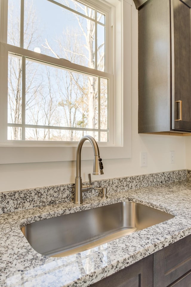 room details featuring dark brown cabinets, light stone counters, and sink