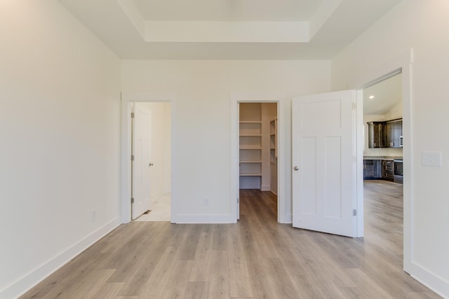 unfurnished bedroom featuring light wood-type flooring, a walk in closet, a closet, and a tray ceiling