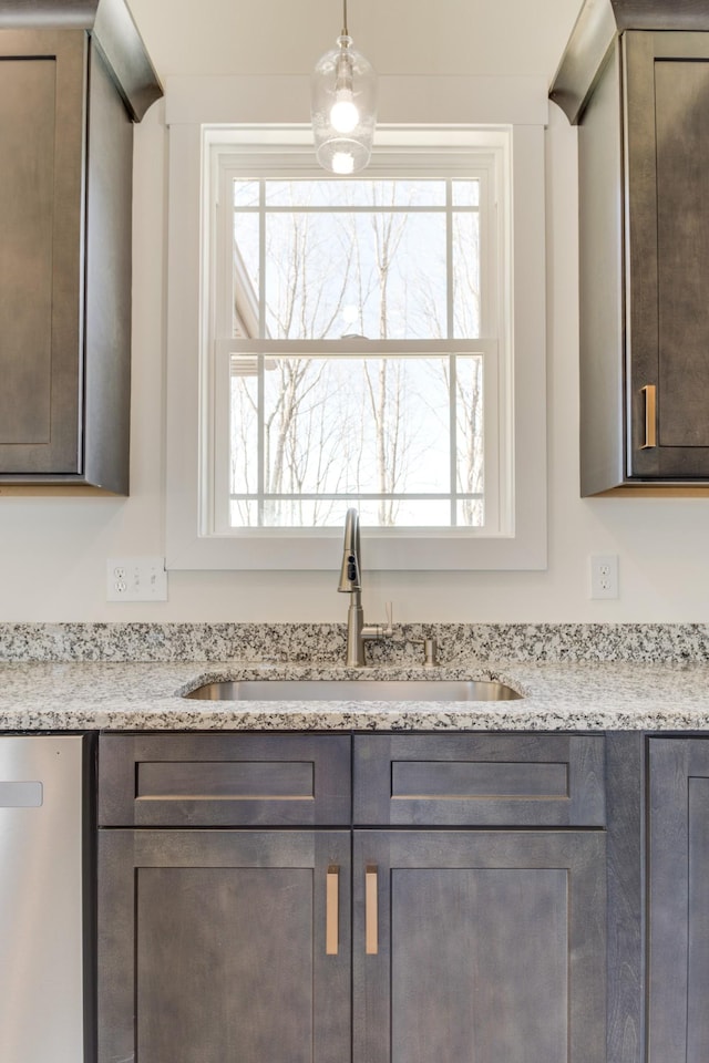 room details featuring dark brown cabinetry, light stone counters, hanging light fixtures, and sink