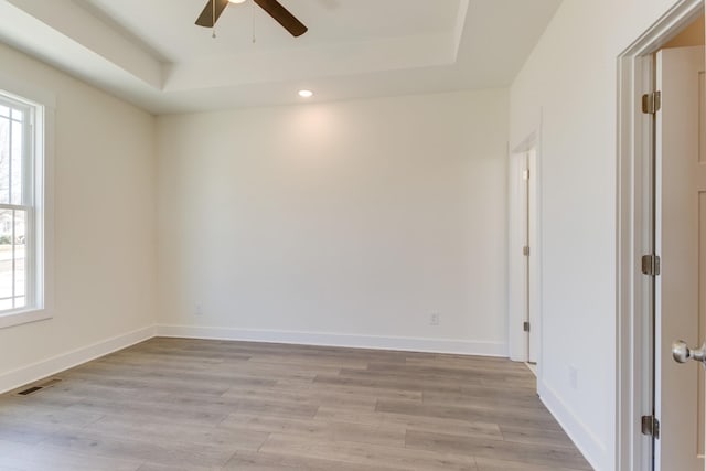 unfurnished room with ceiling fan, light hardwood / wood-style floors, and a tray ceiling