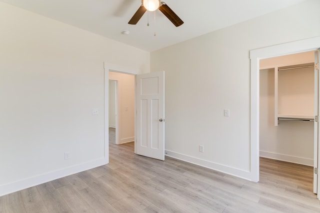 unfurnished bedroom featuring ceiling fan, a closet, a walk in closet, and light wood-type flooring