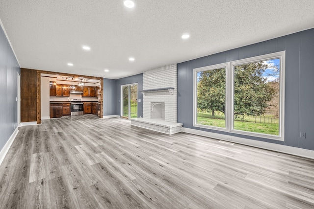 unfurnished living room with a brick fireplace, wood walls, a textured ceiling, and light hardwood / wood-style flooring