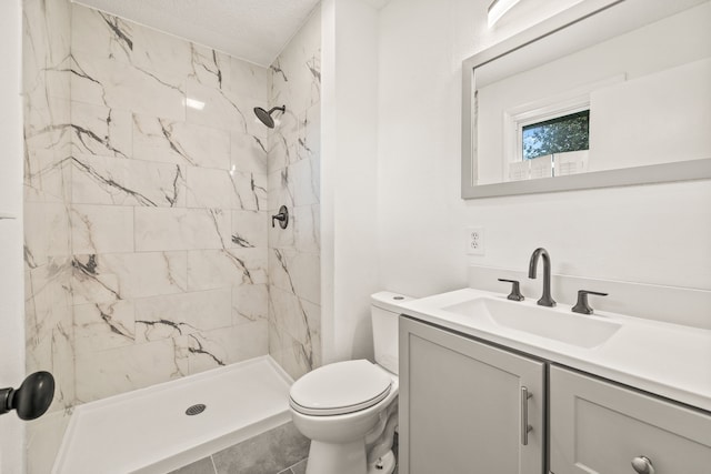 bathroom with vanity, toilet, a textured ceiling, and tiled shower