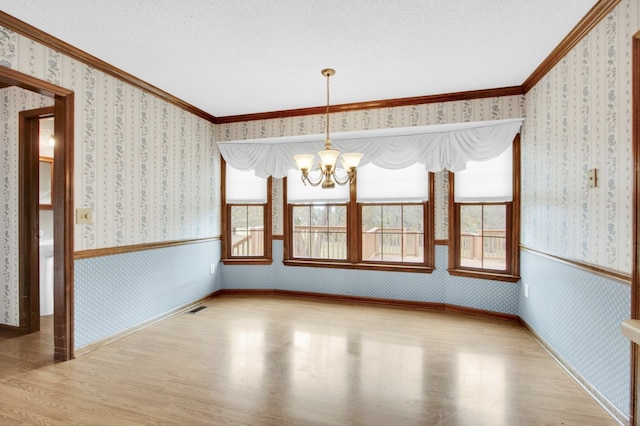 unfurnished dining area with hardwood / wood-style flooring, a chandelier, a textured ceiling, and ornamental molding