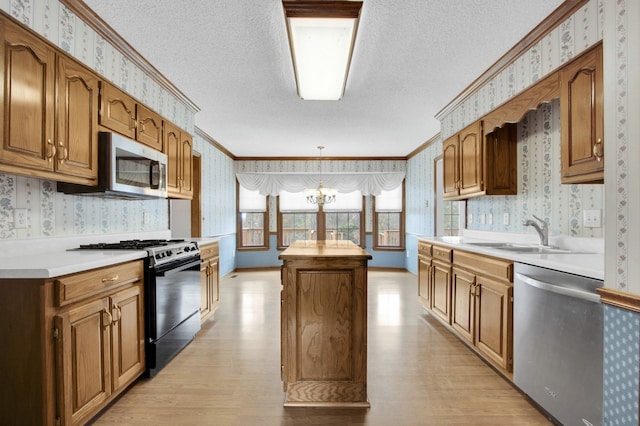 kitchen with ornamental molding, stainless steel appliances, a kitchen island, light wood-type flooring, and sink