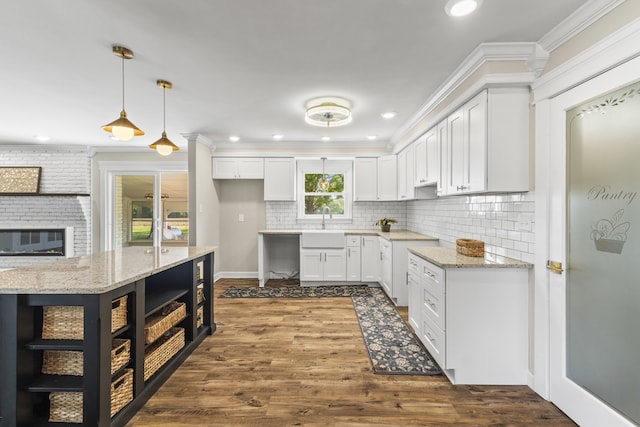 kitchen with light stone counters, white cabinets, dark hardwood / wood-style floors, crown molding, and pendant lighting