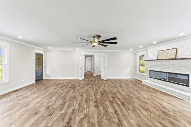 unfurnished living room featuring a brick fireplace, light wood-type flooring, ceiling fan, and crown molding