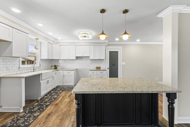 kitchen featuring crown molding, a kitchen island, light stone countertops, white cabinets, and dark wood-type flooring