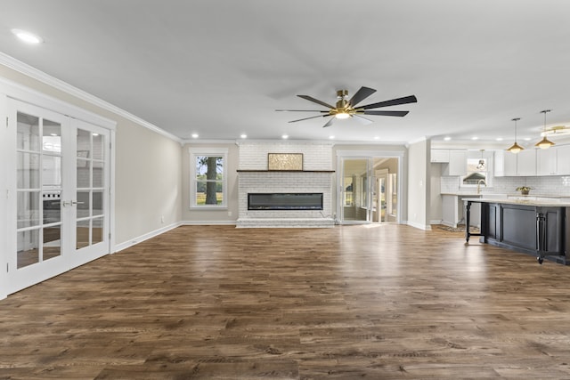 unfurnished living room featuring french doors, crown molding, dark hardwood / wood-style floors, a brick fireplace, and ceiling fan