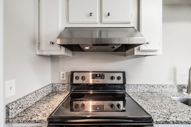 kitchen with wall chimney range hood, sink, electric range, light stone counters, and white cabinetry