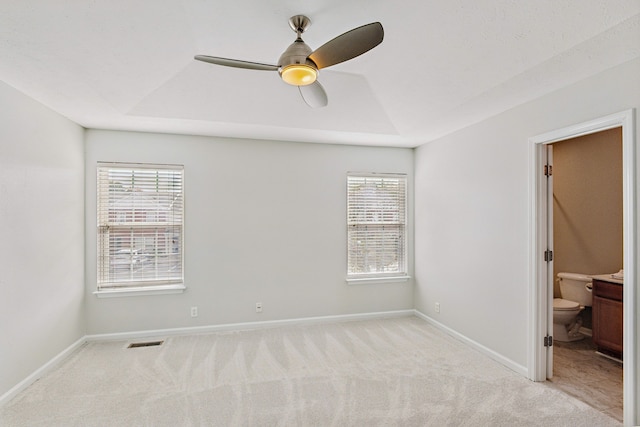 unfurnished bedroom with ceiling fan, connected bathroom, light carpet, and a raised ceiling