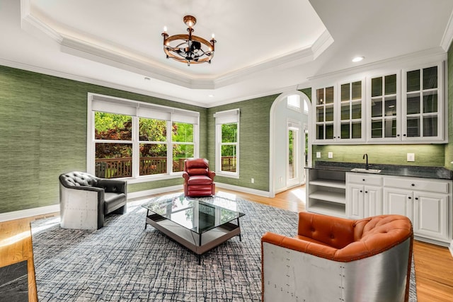 living room featuring crown molding, a notable chandelier, wet bar, light hardwood / wood-style floors, and a tray ceiling