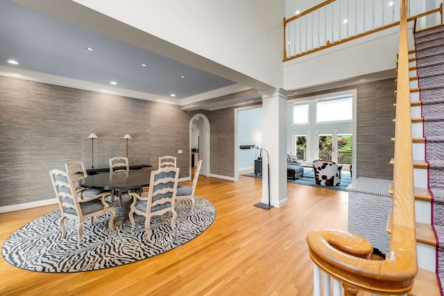 dining space with a towering ceiling, light wood-type flooring, and crown molding