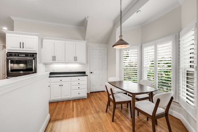 kitchen with ornamental molding, stainless steel oven, pendant lighting, white cabinets, and light hardwood / wood-style flooring