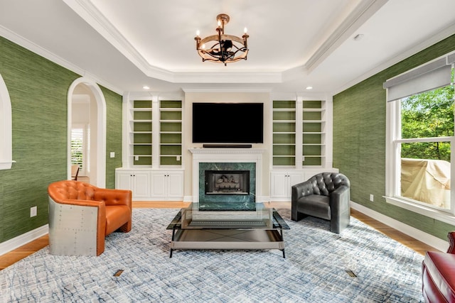 living room with ornamental molding, hardwood / wood-style floors, a fireplace, a raised ceiling, and built in features