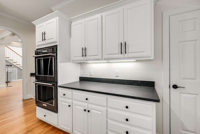 kitchen with white cabinetry, light hardwood / wood-style floors, ornamental molding, and double oven