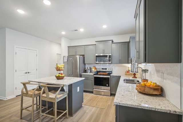 kitchen featuring light stone counters, stainless steel appliances, a kitchen island, sink, and light hardwood / wood-style floors