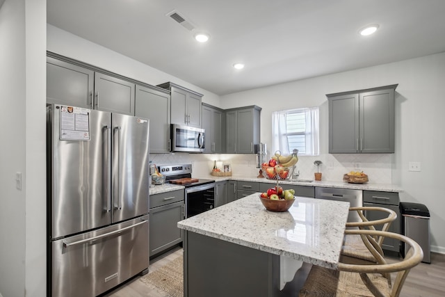 kitchen with light hardwood / wood-style floors, appliances with stainless steel finishes, light stone countertops, a breakfast bar area, and a center island