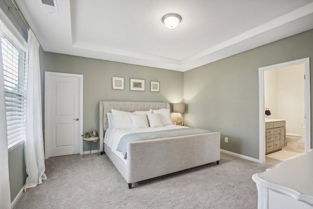 bedroom featuring ensuite bath, light colored carpet, and a tray ceiling