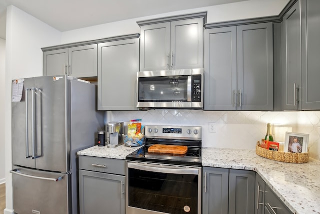 kitchen featuring gray cabinets, light stone countertops, backsplash, and stainless steel appliances