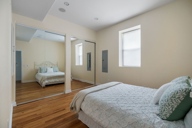 bedroom featuring electric panel, hardwood / wood-style floors, and two closets