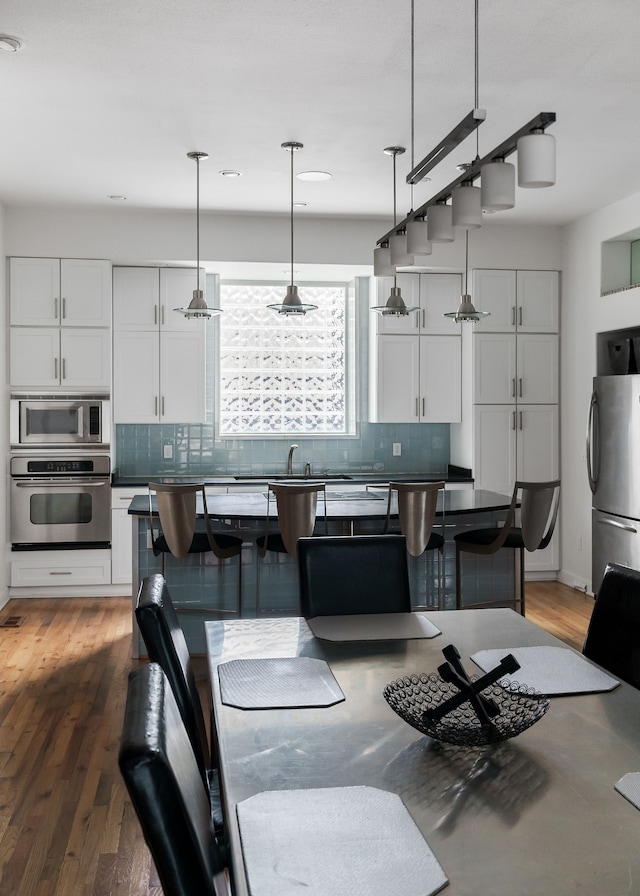 kitchen featuring stainless steel appliances, dark hardwood / wood-style floors, hanging light fixtures, white cabinets, and decorative backsplash