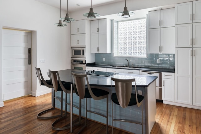 kitchen with a center island, hardwood / wood-style floors, white cabinetry, appliances with stainless steel finishes, and decorative light fixtures