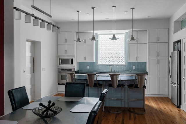 kitchen featuring stainless steel appliances, light hardwood / wood-style floors, white cabinetry, and decorative light fixtures