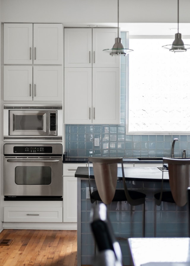 kitchen featuring white cabinetry, stainless steel appliances, and decorative light fixtures