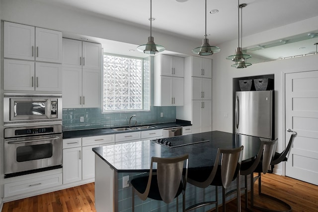 kitchen with stainless steel appliances, wood-type flooring, white cabinets, and pendant lighting