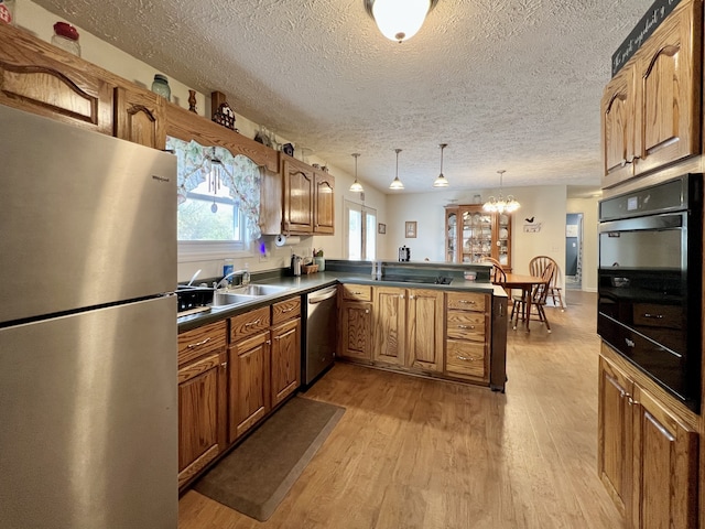 kitchen featuring sink, light hardwood / wood-style flooring, appliances with stainless steel finishes, decorative light fixtures, and kitchen peninsula