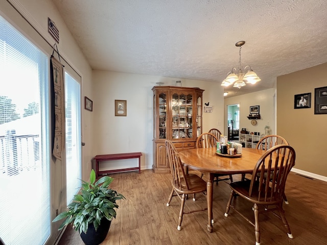 dining room with a textured ceiling, an inviting chandelier, and light hardwood / wood-style flooring