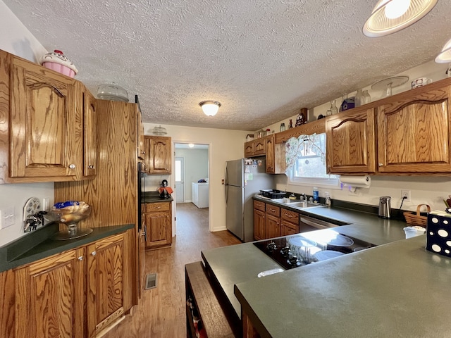 kitchen featuring sink, stainless steel appliances, independent washer and dryer, light hardwood / wood-style floors, and a textured ceiling