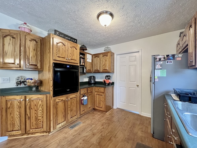 kitchen with sink, light hardwood / wood-style flooring, black oven, stainless steel fridge, and a textured ceiling