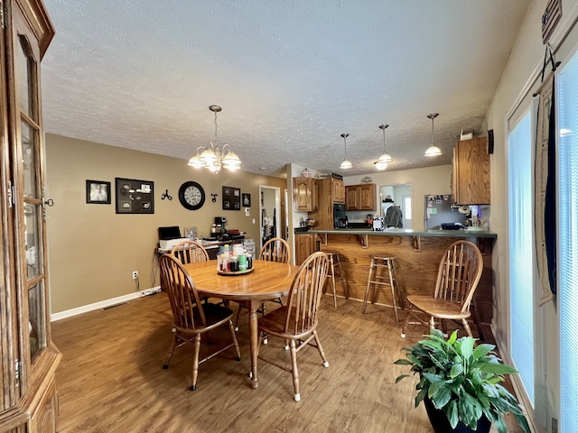 dining area with a notable chandelier, light hardwood / wood-style flooring, and a textured ceiling