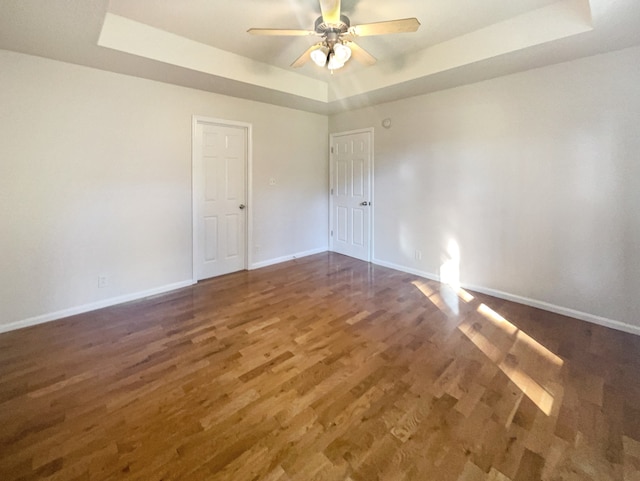 unfurnished room with ceiling fan, a raised ceiling, and dark hardwood / wood-style flooring