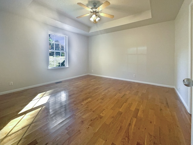 empty room featuring wood-type flooring, ceiling fan, and a raised ceiling