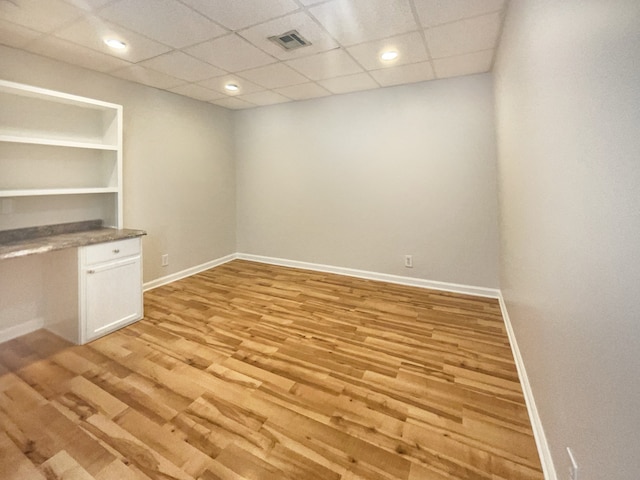 unfurnished room with light hardwood / wood-style flooring, a paneled ceiling, and built in desk