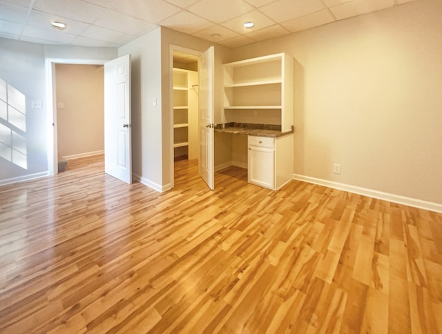 unfurnished living room with light hardwood / wood-style flooring, a paneled ceiling, and built in desk