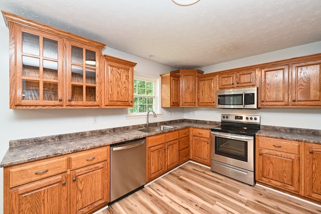 kitchen featuring a textured ceiling, appliances with stainless steel finishes, sink, and light hardwood / wood-style flooring