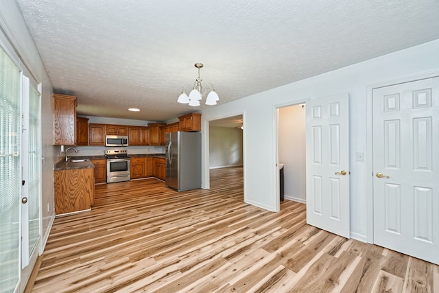 kitchen featuring stainless steel appliances, sink, an inviting chandelier, decorative light fixtures, and light wood-type flooring