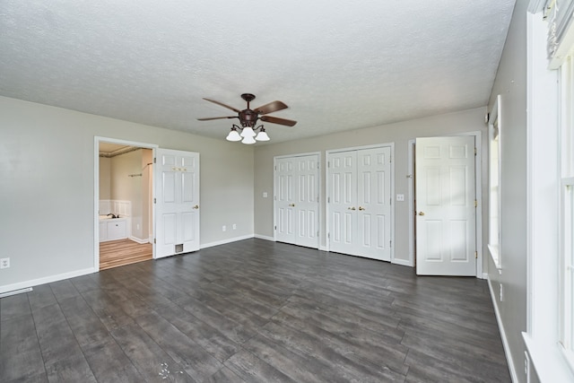 unfurnished bedroom featuring a textured ceiling, dark hardwood / wood-style flooring, multiple closets, ceiling fan, and ensuite bathroom