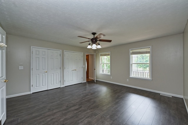 unfurnished bedroom with a textured ceiling, dark hardwood / wood-style floors, ceiling fan, and two closets