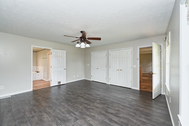 unfurnished bedroom with ensuite bath, ceiling fan, a textured ceiling, dark hardwood / wood-style flooring, and two closets