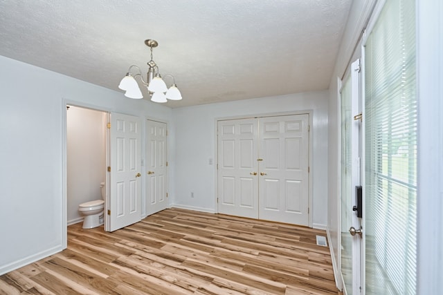 unfurnished bedroom featuring a textured ceiling, a chandelier, connected bathroom, two closets, and light wood-type flooring