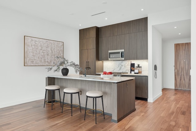 kitchen with tasteful backsplash, a kitchen island, sink, light hardwood / wood-style floors, and a breakfast bar